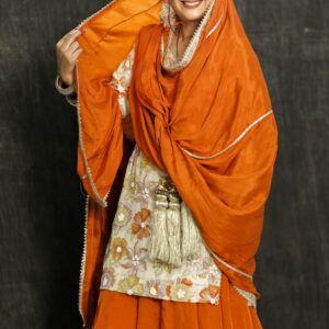 Smiling woman in vibrant Punjabi attire posing with orange dupatta, showcasing cultural elegance.